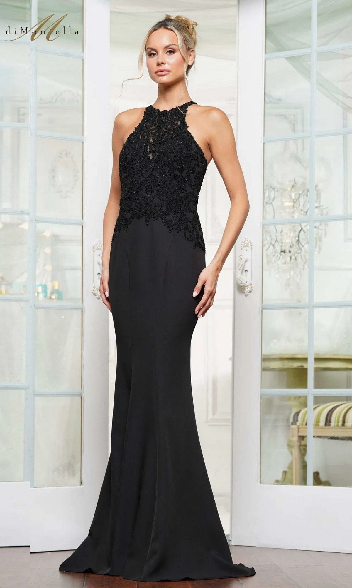 A woman stands indoors wearing the Long Formal Dress: Rina Di Montella RD3243 in black, a sleeveless, floor-length gown with a delicate lace-embroidered bodice.